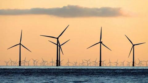 A series of wind turbines over the sea at sunset.