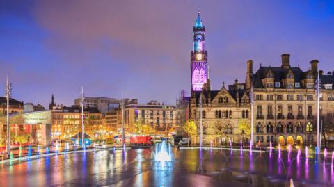 Dramatic night shot of Bradford Town Hall reflected in the mirror pool in the city park.