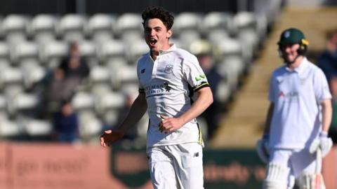 Tom Price celebrates after taking a wicket for Gloucestershire, wearing an all-white kit, with a batter in the background