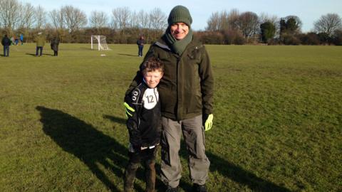 A picture of a young rather muddy boy on a football pitch with his Dad with his arm around him 