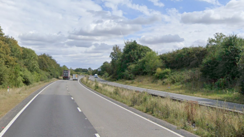 The A14 dual carriageway is seen in the picture. On the left-hand carriageway is one lorry and a van overtaking it, heading away from the camera.  Across the other side of the road is a van travelling towards the camera. 