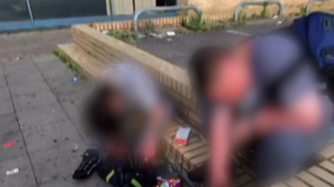 Image shows people sitting on a wall with litter around them. Their faces have been blurred.