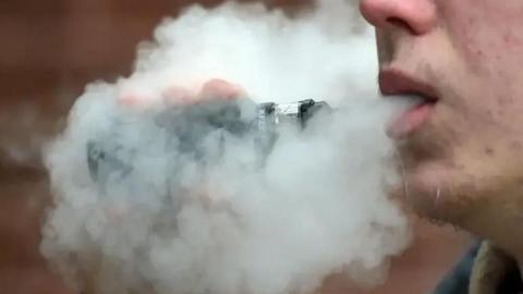 A closeup of a plume of smoke coming from a man's mouth as he vapes.