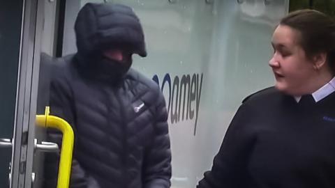 Christopher El Gifari in handcuffs, his face mostly hidden by the hood of a puffy black jacket is let out of a police van