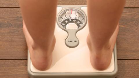 Someone is standing on a set of bathroom scales with two bare legs. There is a measure in the centre of the scales with various numbers around it.