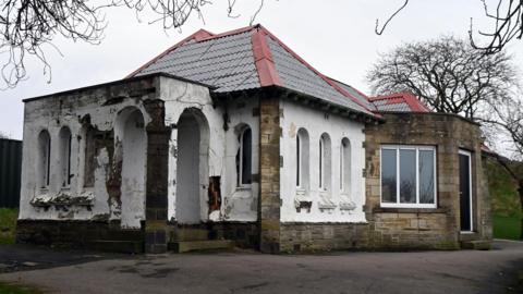 A small stone building with a white-painted entrance porch area. It is run down and seems to not be in use.