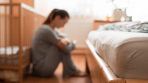 Blurred image of woman sat on the floor near a cot and a bed