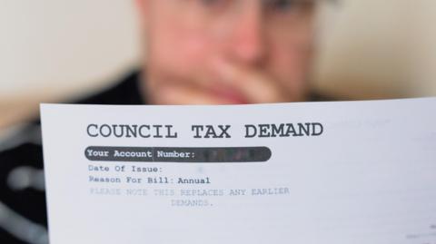 A worried looking man, holding his hand over his mouth, is blurred in the background. In the foreground is a white sheet of paper with the words "council tax demand" in large capital letters at the top