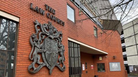The front of Swindon courts - a large red brick building, some tree branches in front on a grey day