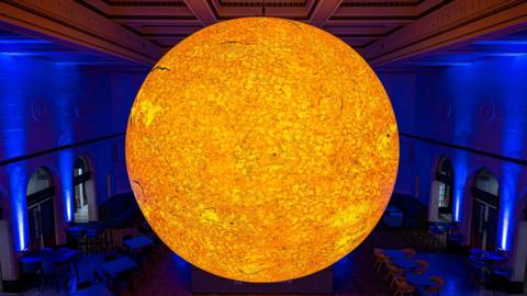 A large bright warm yellow ball which resembles the sun in a blue lit room