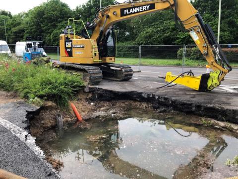 Digger next to a hole in a road full of water