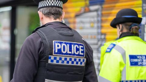 Two police officers walking away from the camera side by side.