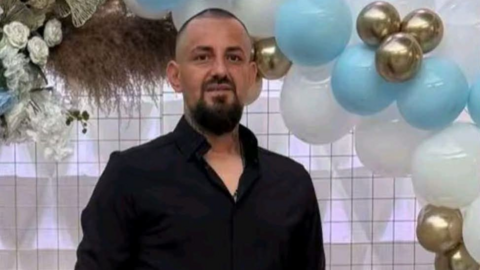 A man in a black shirt stood in front of a checkered wall and a balloon arch