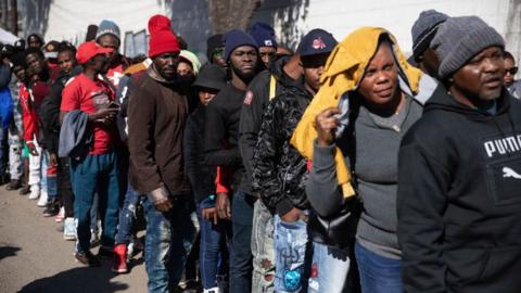 Migrants from Haiti and other Latin American countries standing in a long queue 