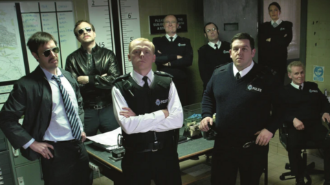 The actors from Hot Fuzz posing in police uniforms inside a police station. They are looking into the camera.