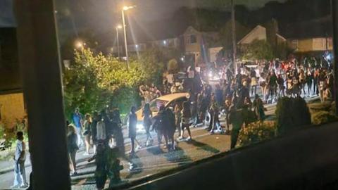 A huge crowd of people seen through a window walking through a residential street. 