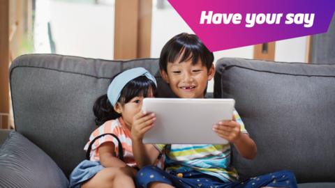 children looking at tablet while sat on sofa. 
