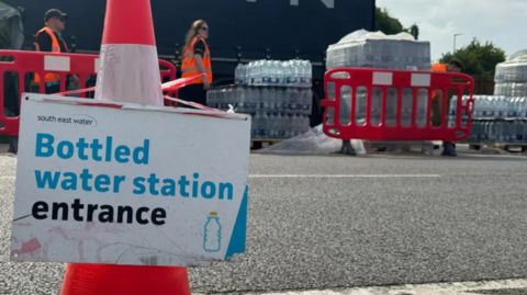 A sign advertising the entrance to a bottled water station near Whitstable, Kent. South East Water workers can be seen in the background of the image.