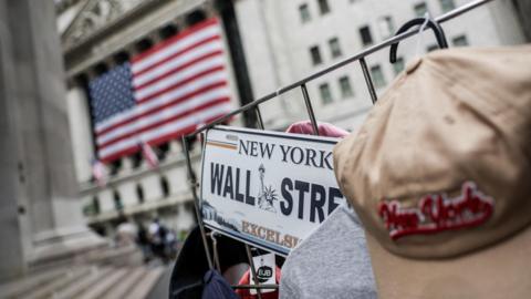 A Wall Street sign in front of a large American flag in New York