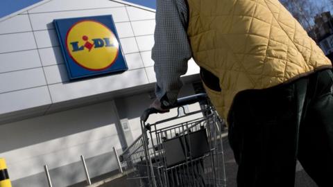 A man pushes a shopping trolley towards a large Lidl supermarket