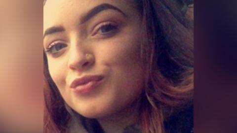 Tasha is a young woman with brown hair and green eyes. She is smiling at the camera.