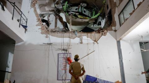 An official looks up with his arms behind his back and back turned to the camera, as they inspect a huge hole in the wall of a building interior, with some of the plane visible in the hole, on Thursday.