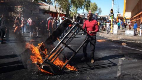 A man lifts a burning piece of furniture during a riot in the Johannesburg suburb of Turffontei