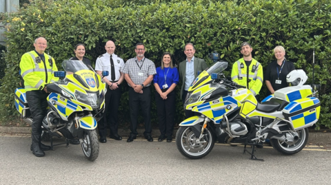 A line-up of eight people standing next to special motorbikes, including Matthew Barber, who is the third person from the right.