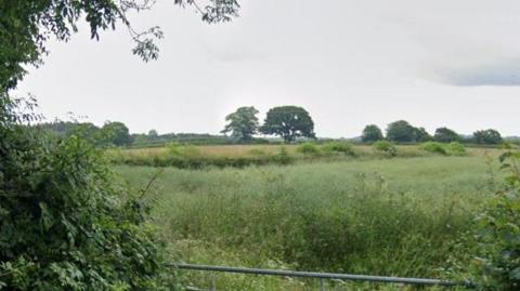 A large green field with a hedgerow separating it from other fields