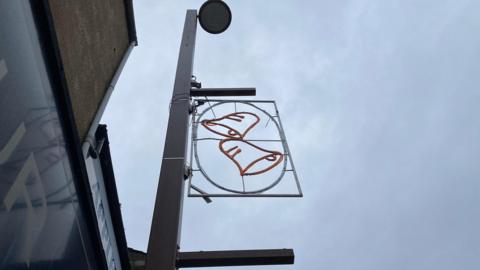 Christmas lights depicting jingle bells are attached to a light post. The design is not illuminated in this picture.