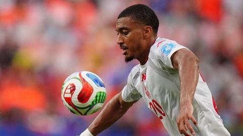 Yan Valery in white Tunisia playing kit and the number 20 in the middle of the shirt written in red controls a bouncing ball