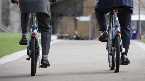 Two men cycling wearing suits cycling on a city street