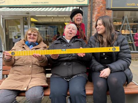 Three women sat on a bench holding a spirit level