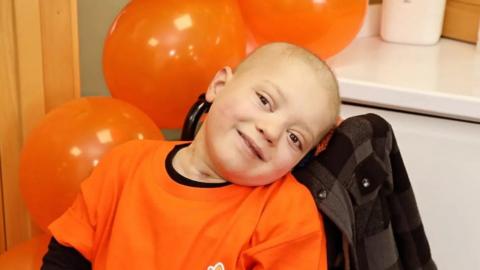 Young boy in orange t-shirt surrounded by balloons