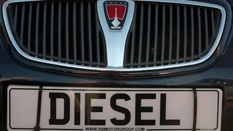 A diesel sign is displayed on the front of a second hand car for sale parked on a used car lot