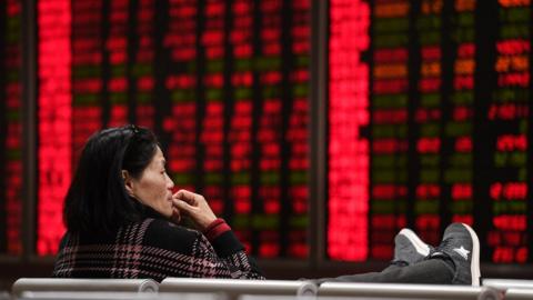 A woman looks at boards showing stock prices at a securities company on the first trading day of the year in Beijing on January 2, 2018