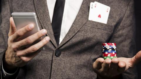 A man in a suit holding poker chips and a smartphone