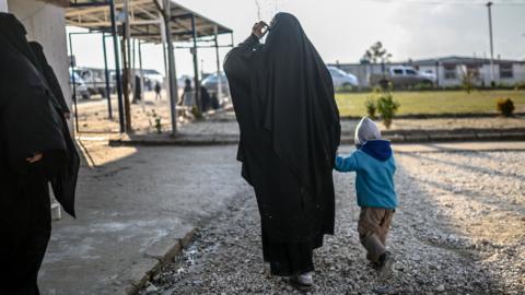 A woman walks with her child at a camp in northeastern Syria