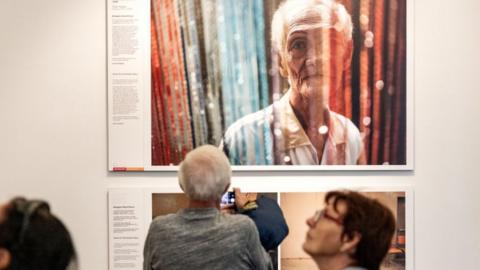 A man takes a photo of an exhibited photograph by Hannah Reyes Morales