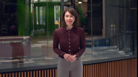 Catrin Haf Jones, a young woman with shoulder length dark hair stand in front of a TV studio