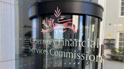 A revolving door in the reflection of a window. It has a logo saying “Guernsey Financial Services Commission”.