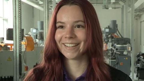 Ellie Ford, with reddish hair, is pictured standing in front of machinery at the institute