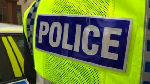 Close up of an officer wearing a high vis vest with 'police' written on the back