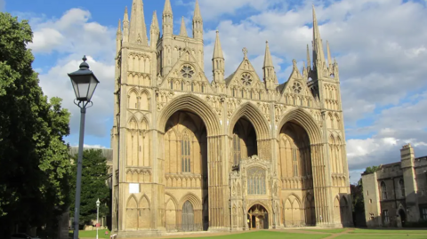 Exterior picture of the historic cathedral with grass laid in front it and a cloudy blue sky.