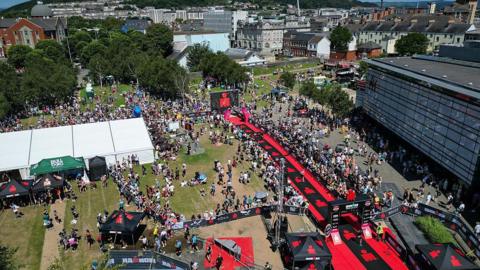 An aerial view of the finish line of Ironman 70.3 Swansea which is the first Pro Series race to be held in the UK. There are swarms of competitors and people watching on the with city skyline in the background