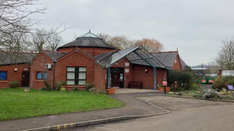 A GP surgery's main entrance, with some grass and a road
