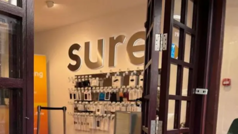 The inside of a Sure broadband provider shop. The word 'Sure' is emblazoned on the wall, above a collection of mobile phone accessories.