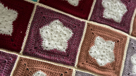A shot of a section of one of the blankets showing purple and orange squares with white flower designs and white bordering