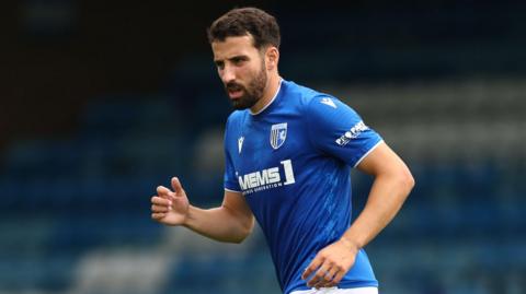 Nick Freeman jogs while on the pitch during a pre-season game for Gillingham. He is wearing a blue Gillingham team shirt.