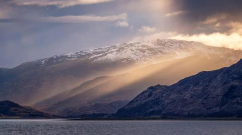 In an atmospheric image of snow capped hills on the shores of Loch Linnhe.